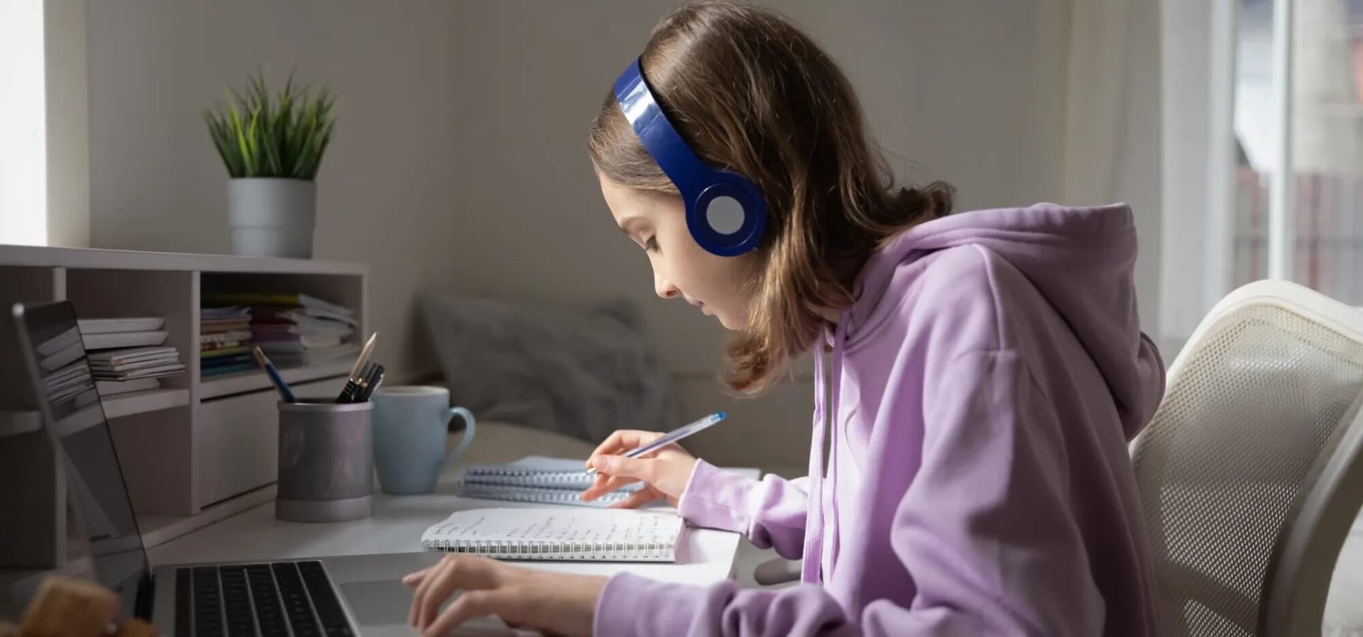 Middle school student with headphones taking notes beside a laptop